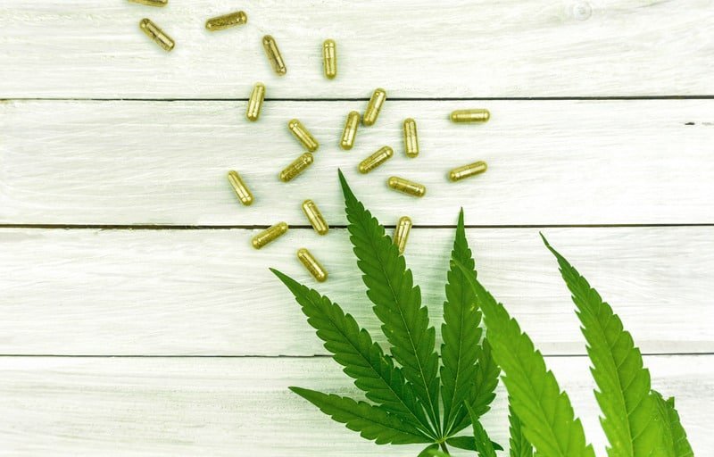 Canva CBD Pills. Group of Clear CBD Cannabidiol Capsules on Bright Wooden Backdrop with Hemp Leafs