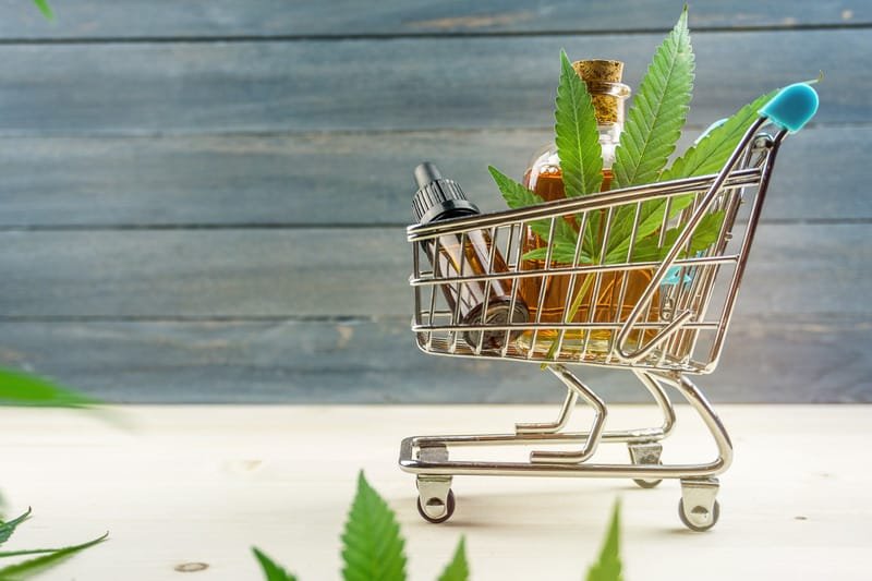 Canva Supermarket Trolley with Marijuana Leafs and Medical Cannabis Oil Cbd on Wooden Backdrop